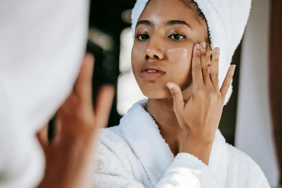 A girl with a towel on her head putting skin care on her cheek.